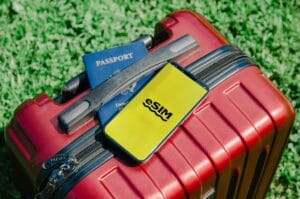 Close-up of a red suitcase with a smartphone displaying eSIM and a passport, symbolizing travel readiness.