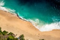 Stunning aerial view of Bali's beach with turquoise waves crashing on golden sand.